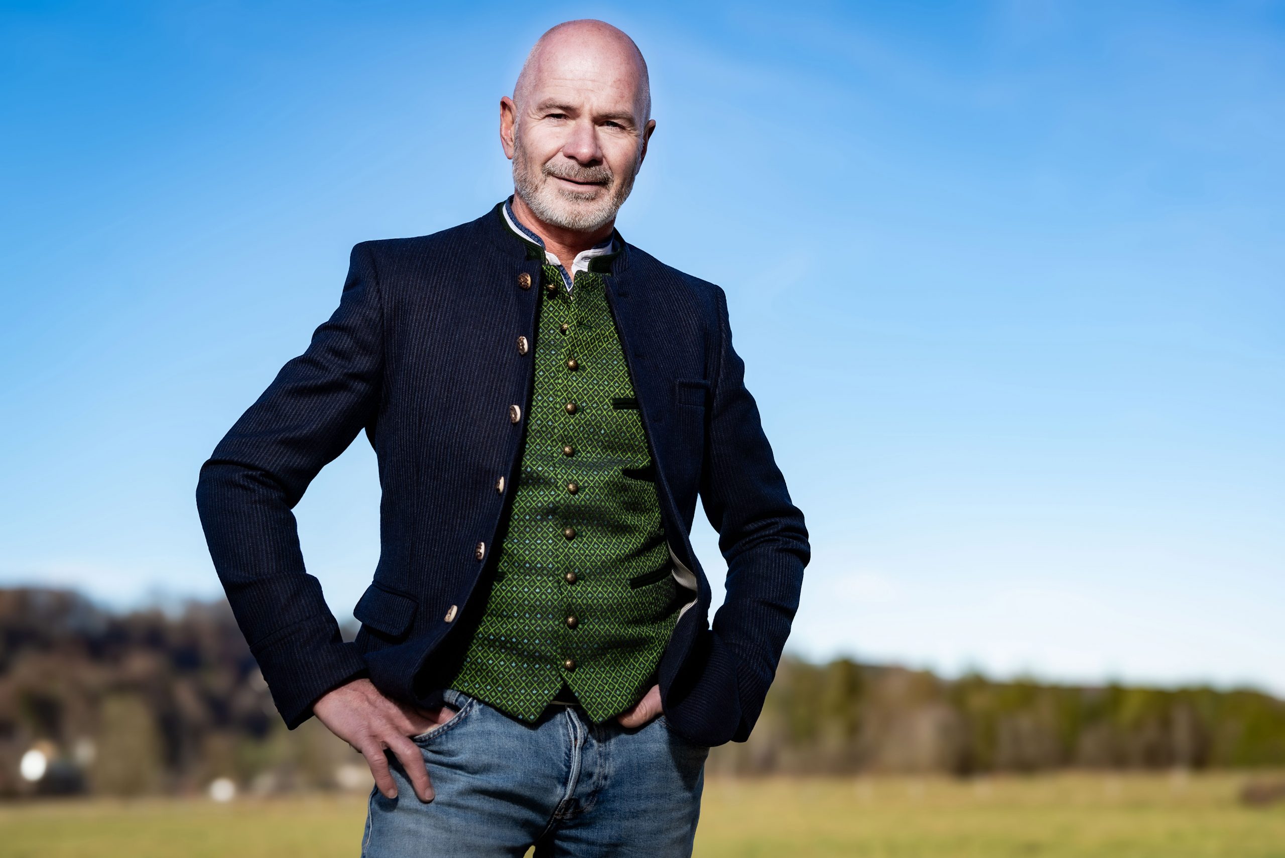 Klaus Heilinglechner in traditioneller Tracht mit grünem Weste und schwarzem Sakko, steht mit Händen in den Taschen im Freien.